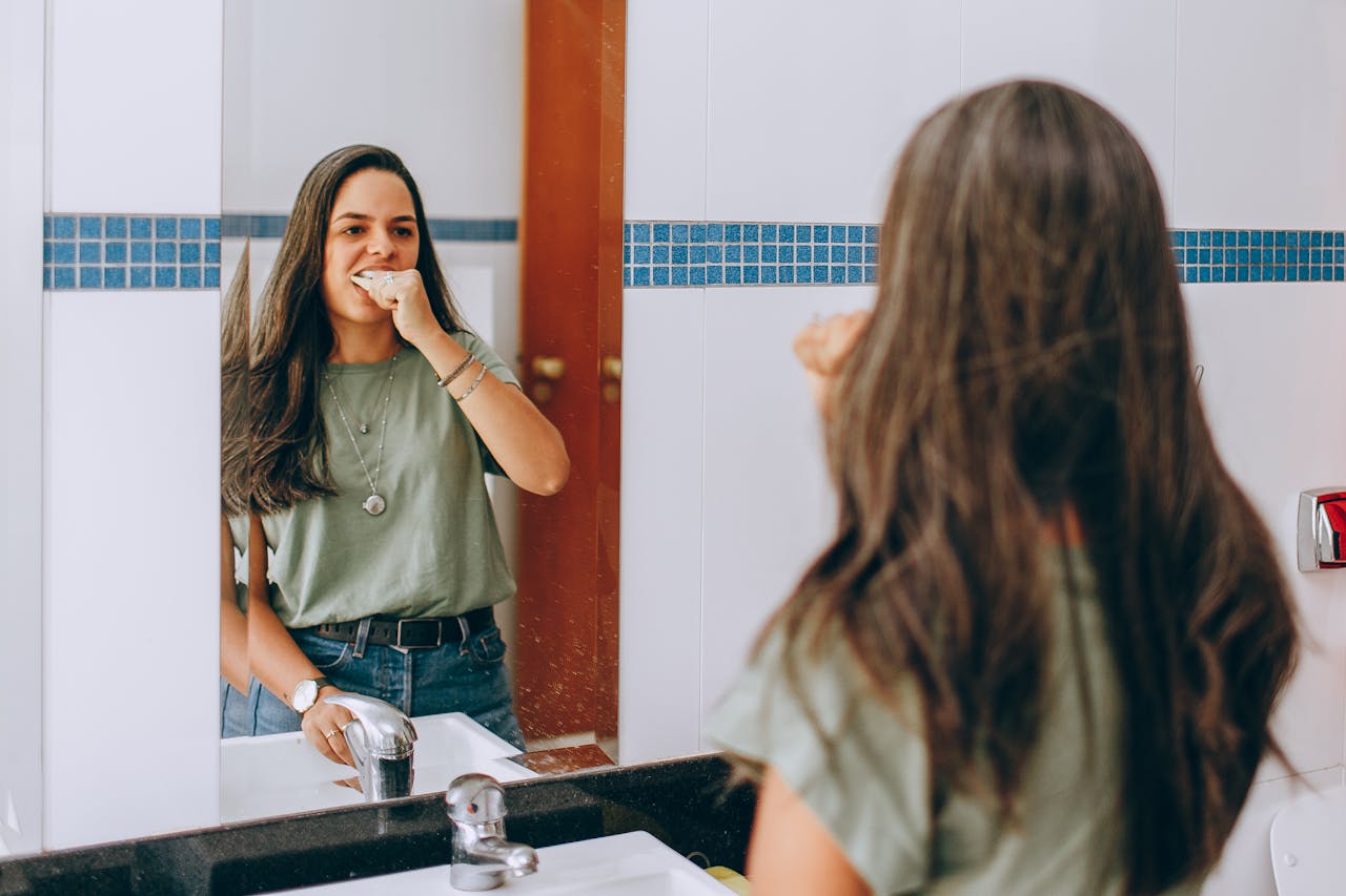 Teen brushing teeth in a bathroom mirror as part of a post-meal oral hygiene routine while using clear aligners